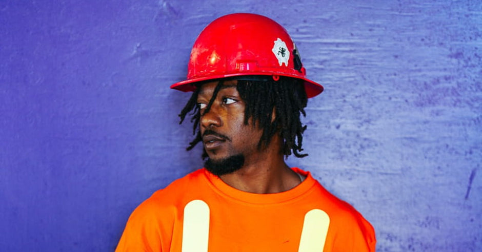 A man wearing a hard hat and an orange high-visibility t-shirt with reflective stripes on the front and on the sleeves.