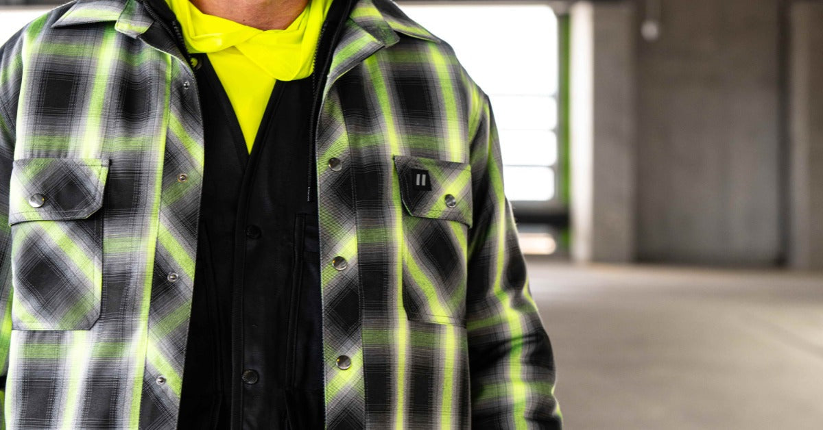 A close-up of a man wearing a hard hat, work gloves, and a few top layers with high-visibility materials.