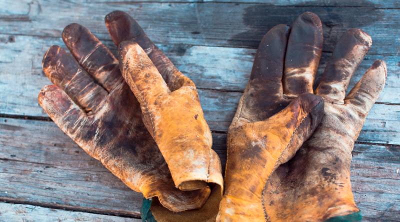 Dirty old work gloves on a wooden table stained with grease and oil showing the marks of hard work and dedication. 