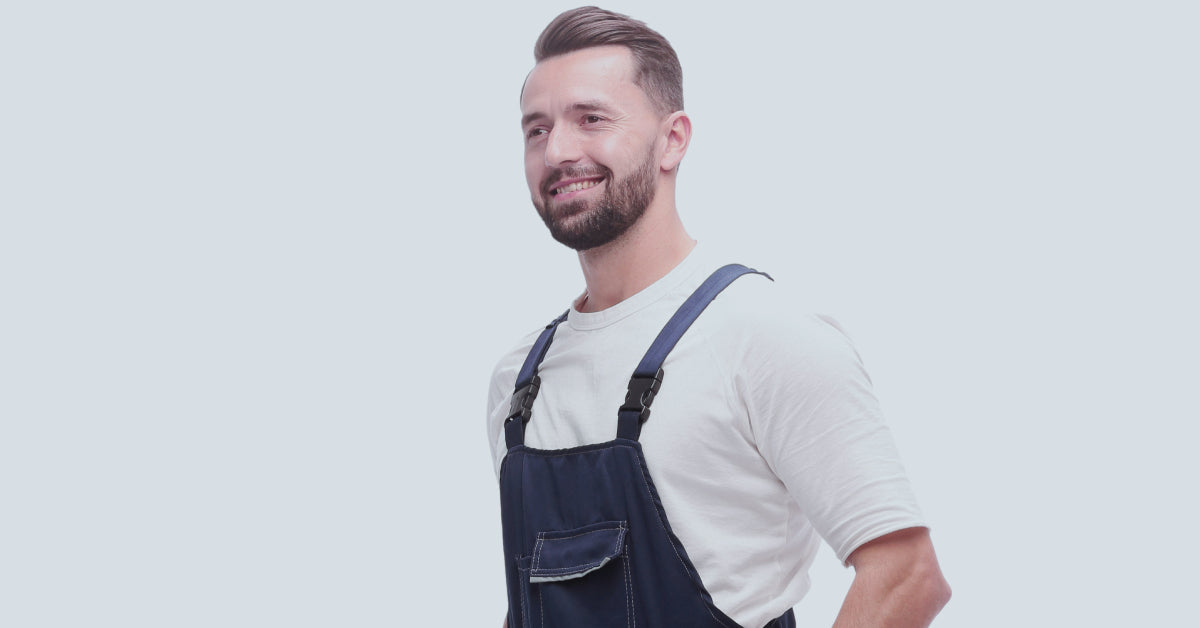 A smiling man wearing overalls, looking forward with a cheerful expression against a plain background.